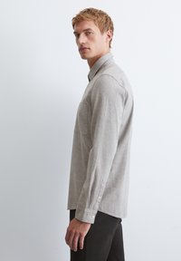 Hellgraues Langarmhemd mit Button-down-Kragen, einer einzelnen Brusttasche und knöpfbaren Manschetten. Der Stoff hat eine subtile Textur.