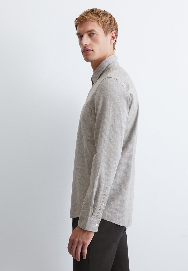 Hellgraues Langarmhemd mit Button-down-Kragen, einer einzelnen Brusttasche und knöpfbaren Manschetten. Der Stoff hat eine subtile Textur.