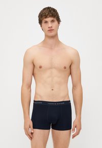 Tengerészkék pamut boxer alsónadrág, egyszínű dizájnnal és rugalmas derékkal, amelyen a "TOMMY HILFIGER" logó fehér és piros részletekkel látható.