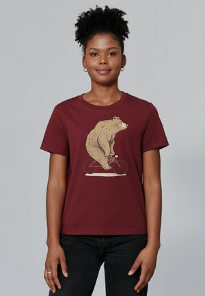 T-shirt bordeaux avec une illustration d'un ours faisant du vélo. Le tissu est en coton, avec un col rond et des manches courtes.
