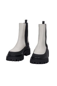 Masivní kotníkové boty z bílé a černé kůže, které mají texturovanou platformu, elastické boční panely a poutko pro snadné obouvání.