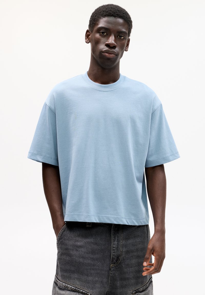 T-shirt in cotone azzurro chiaro con vestibilità rilassata, maniche corte e scollo rotondo. Indossato con pantaloni corti in denim grigio scuro e larghi.