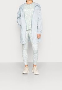 Ljusblå regnjacka med huva, i kombination med en mintgrön top med blommönster och leggings. Avslutad med krämfärgade sneakers.