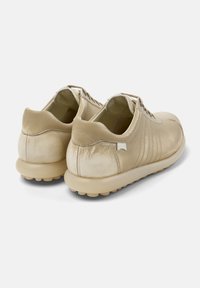 Zapatos de cuero beige con una textura suave, forma redondeada y suela de goma blanda, con costuras sutiles y detalles de marca.