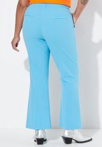 Pantalons évasés bleu clair avec une texture lisse, dotés de deux poches arrière et d'une ceinture, complétés par des bottes à talons argentées.