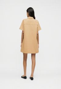 Φόρεμα με κοντά μανίκια και γιακά από ανοιχτό καφέ ύφασμα, με ίσια γραμμή, ραφή στο πίσω μέρος και συνδυασμένο με μαύρα επίπεδα παπούτσια.