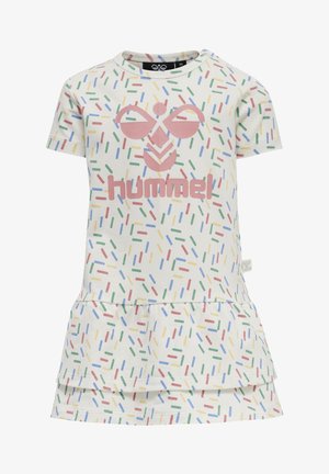 Kjol i bomull med en krämfärgad bakgrund och färgglada strösselmönster. Fram har den en rosa logotyp med en volangkant som accent.
