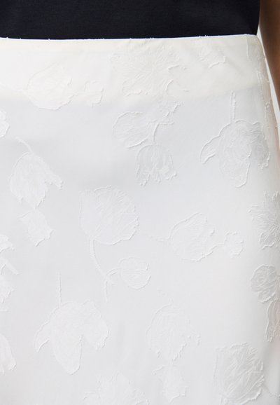 Falda blanca con un patrón floral en relieve y una textura suave. Presenta detalles sutiles y una cinturilla suave. Adecuada para diversas ocasiones.