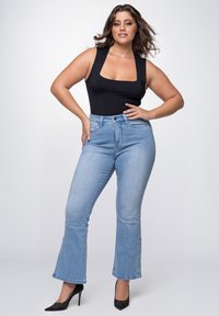 Schwarzer ärmelloser Body, hochtaillierte hellblaue Schlagjeans und schwarze spitze Absätze. Glatte Textur, definierte Silhouette, klassischer Denim.