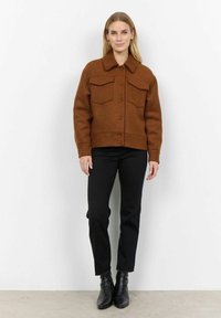 Veste en mélange de laine marron avec un col, deux poches poitrine et fermeture à boutons à l'avant, associée à un pantalon noir ajusté et des bottines.