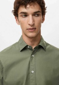 Hellolivgrünes Hemd zum Knöpfen mit glatter Textur, spitzem Kragen und grauen Knöpfen, mit lockerem Schnitt und ohne sichtbare Muster.