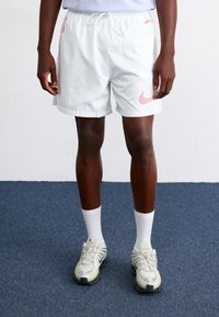 Bijele kratke hlače s crvenim detaljima, elastičnom uplitnom trakom i vezicom; nosi se s bijelim čarapama do gležnja i sivim sportskim cipelama. Tekstura tkanine.