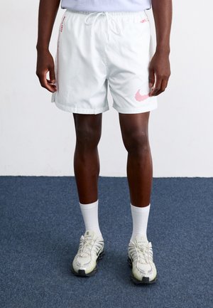 White shorts with red accents, elastic waistband, and drawstring; worn with white crew socks and gray athletic shoes. Textured fabric.