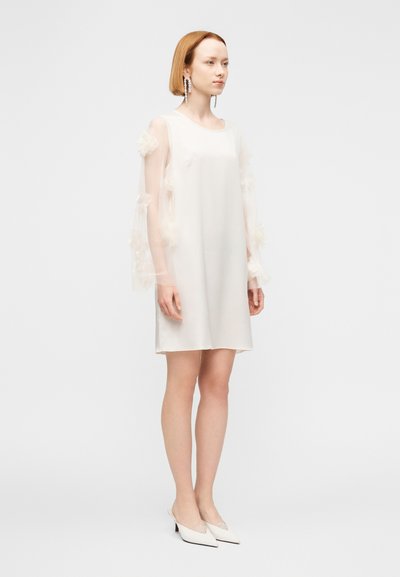 Λευκό φόρεμα με διαφανείς, βολάν μανίκια, στρογγυλή λαιμόκοψη και χαλαρή εφαρμογή. Συνδυασμένο με λευκές γόβες μυτερές, δημιουργώντας μια μίνιμαλ εμφάνιση.