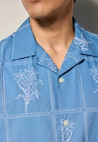 Blauwe short-sleeve shirt van lichtgewicht stof, met witte bloemenborduursels en vierkante stikpatronen, met een klassieke kraag en knoopsluiting.