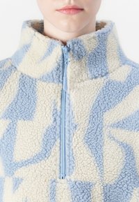 Fleece pullover met een hoge kraag, voorzien van een blauw en crèmekleurig abstract patroon en een rits aan de voorkant. Zacht, gestructureerd materiaal.