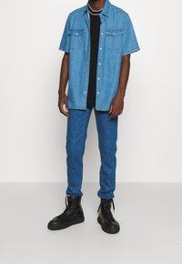 Denimová košile s krátkým rukávem ve světle modré barvě, na knoflíky, s kapsami na hrudi, spárovaná s tmavě modrými skinny džínami a černými vysokými teniskami.