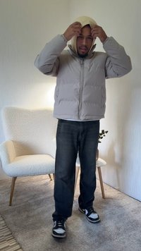 Šviesiai pilka pūkinė striukė su užtrauktuku priekyje, dvi šoninės kišenės. Dėvima ant balto marškinėlio su tamsiais džinsais ir juodais batais. Neutralus fonas.