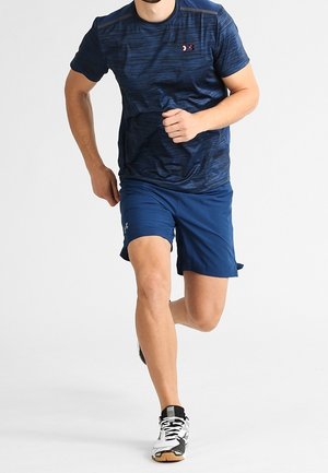 Camiseta deportiva azul marino con patrón texturizado y un pequeño logo, combinada con pantalones cortos azules. Corredor con zapatillas plateadas y negras.