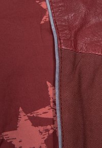 Röd textil med en slät lädersektion och ett tyg med stjärnmönster i en mörkare röd, kantad av en kontrasterande grå söm.