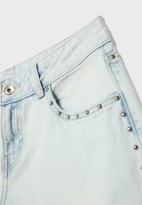 Jean en denim bleu clair avec poche avant ornée de rivets argentés le long du bord de la poche et fermeture par bouton à la taille.
