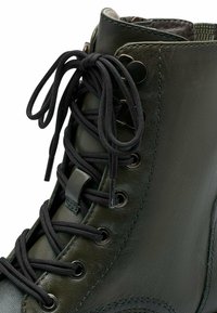 Groene leren enkellaars met zwarte veters, metalen oogjes en een gestructureerde afwerking. Voorzien van een gevoerde kraag en een afgeronde neus.