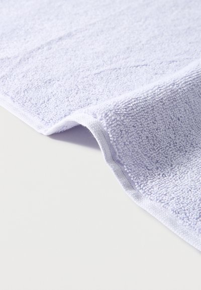 Μαλακή λευκή πετσέτα από περκάλι με καλοραμμένη άκρη, διπλωμένη ελαφρώς πάνω σε απλό φωτεινό φόντο.