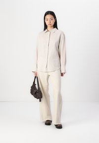 Gai bēša pogājams krekls ar garām piedurknēm, apvienots ar baltiem platiem biksēm. Tumši brūna plecu soma piešķir kontrastu. Gluda tekstūra.