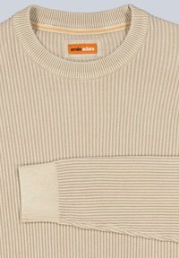 Beige gerippter Pullover mit Rundhalsausschnitt, aus einem strukturierten Stoff. Das Etikett trägt "emilio adani" mit einem orangefarbenen Akzent in der Nähe des Kragens.