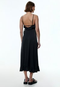 Schwarzes Satin-Kleid mit dünnen Trägern, rüschigem Rücken, knöchellang und mit ausgestellt geschnittenem Saum. Hat eine glatte Textur und ein einfaches Design.