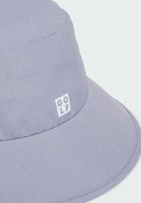 Jasnofioletowa czapka z daszkiem wykonana z gładkiego materiału, z białym prostokątnym logo z napisem "GOLF" z przodu. Zaokrąglony daszek i przeszycia.