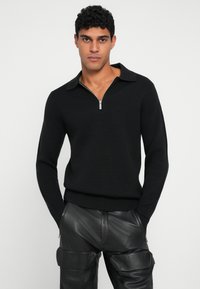 Pulôver preto de malha com gola com zíper e punhos canelados, combinado com calças cargo pretas de couro com múltiplos bolsos.