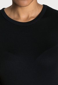 Svart åtsittande t-shirt med rund halsringning, tillverkad av slätt tyg med en subtil glans. Sömmar längs halsringningen.