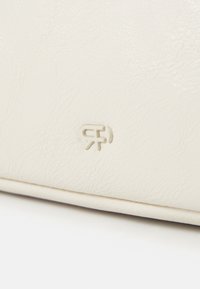 Sac à main couleur crème en faux cuir texturé avec des détails en logo embossés subtils. Présente un design épuré et minimaliste.