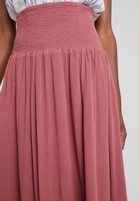 Rosa, fließender Rock mit gesmoktem hoher Taille. Aus strukturiertem Stoff, mit sanften Falten versehen, die eine lässige Silhouette erzeugen.