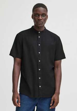 Camisa negra de manga corta con cuello alzado, con un cierre frontal de botones blancos. La tela tiene una textura suave. Diseño simple.