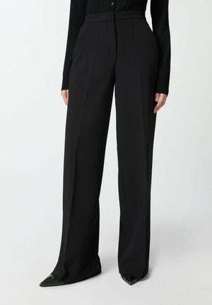 Pantaloni neri su misura con vita alta, frontale plissettato e gambe ampie. Realizzati in tessuto morbido, con una finitura pulita e senza hardware visibile.