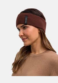 Fascia per la testa in maglia marrone realizzata in materiale morbido, con una texture a coste e un piccolo etichetta nera con "FALKE" ricamata sul lato.