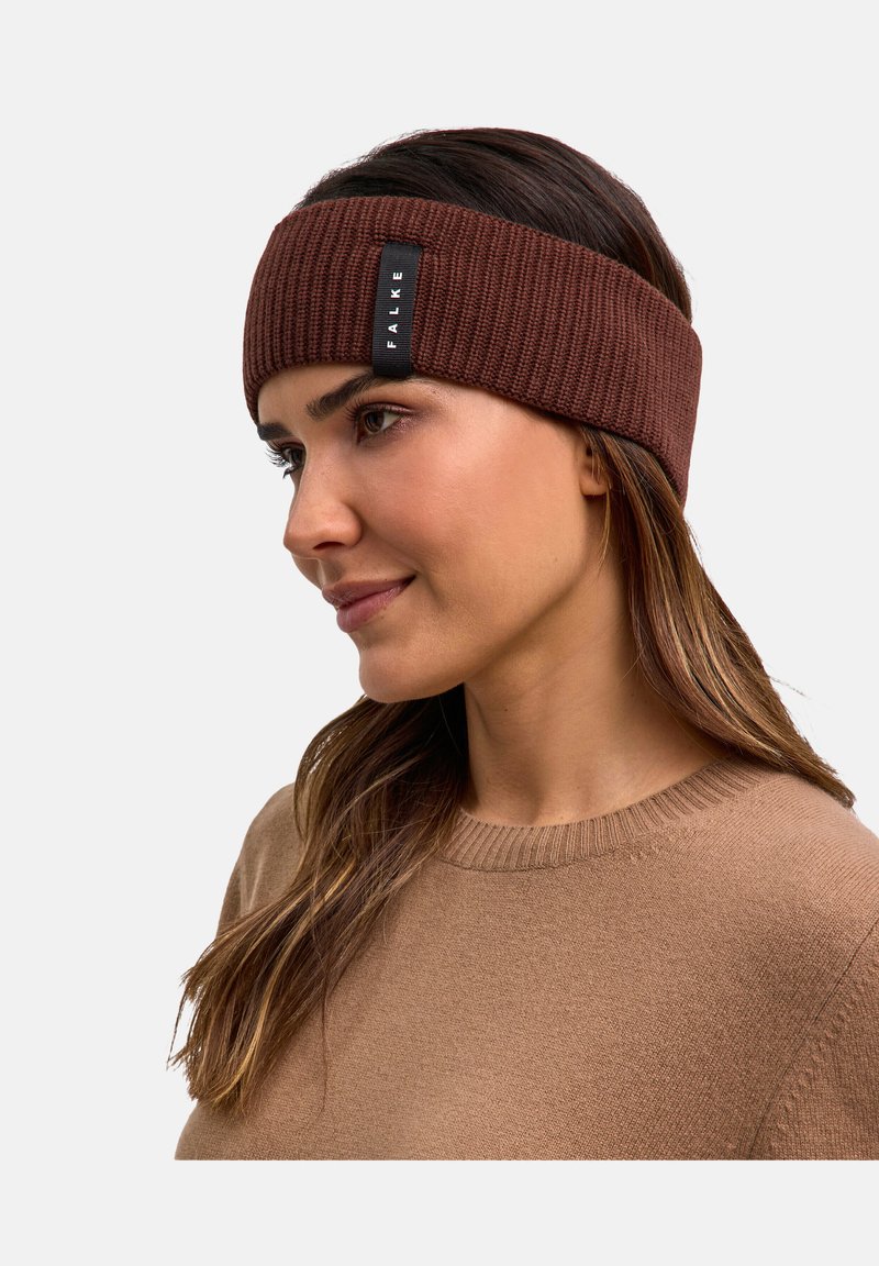 Fascia per la testa in maglia marrone realizzata in materiale morbido, con una texture a coste e un piccolo etichetta nera con "FALKE" ricamata sul lato.