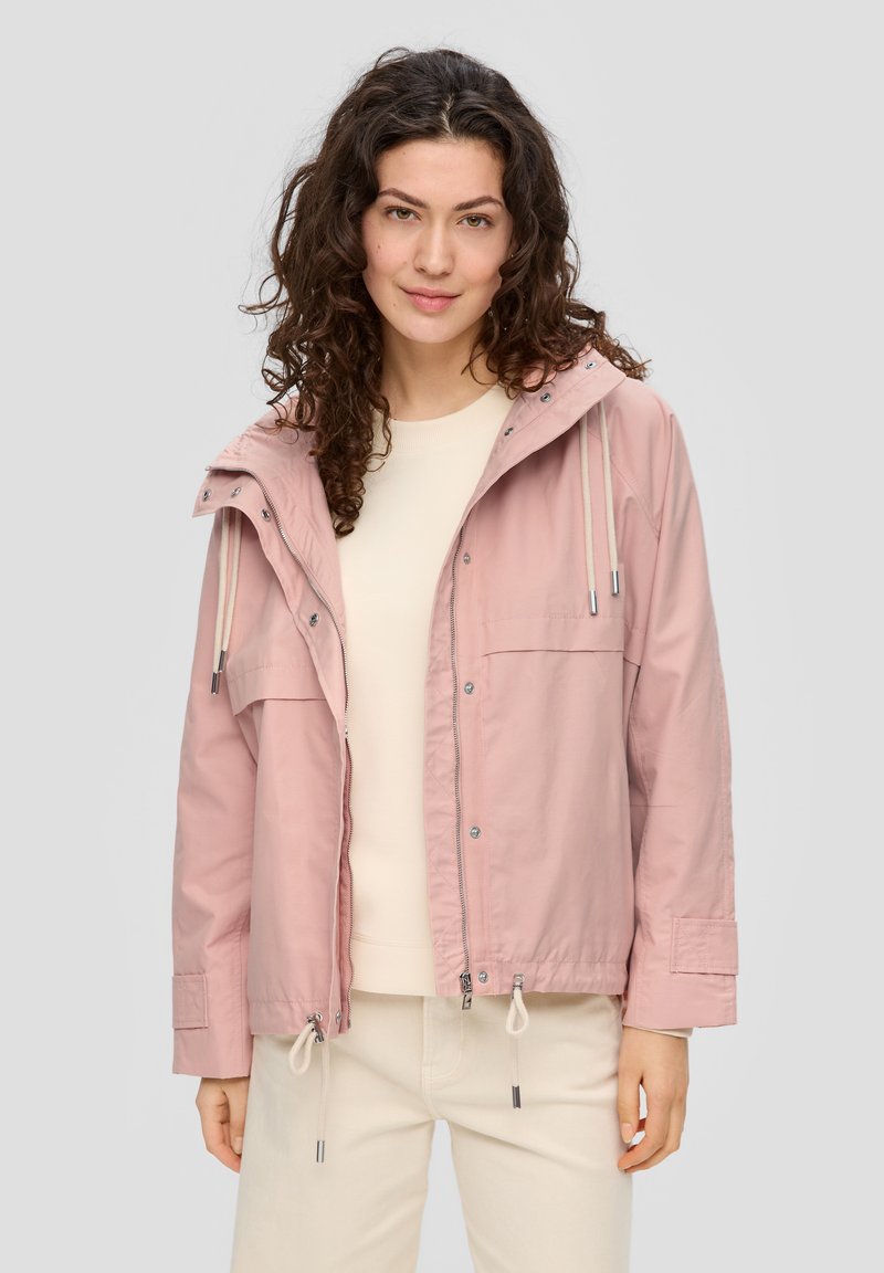 Lichtroze hooded jack met een voorrits, verstelbare trekkoorden, twee borstzakken en elastische manchetten, gedragen over een crèmekleurig top.