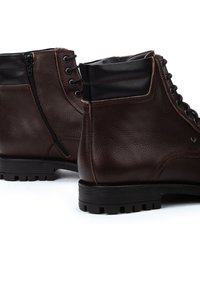 Botas de cuero marrón hasta el tobillo con un acabado texturizado, acentos en negro contrastante, cremallera lateral y suela de goma resistente con patrón de tracción.