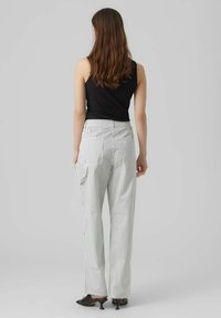 Pantalons larges rayés en blanc et noir avec une taille à cordon et des poches latérales, associés à un débardeur noir ajusté et des mules à talons.