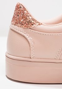 Talons de baskets rose clair en cuir texturé, semelle épaisse et détail pailleté or rose sur la partie arrière du col.