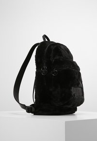 Sac à dos en peluche noir avec un matériau en fourrure texturé, des bretelles ajustables et un logo visible sur la poche avant.