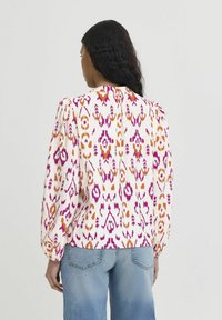 Floral-patterned blouse with long puff sleeves, featuring shades of pink, orange, and cream. Back view shows button detail and relaxed fit.