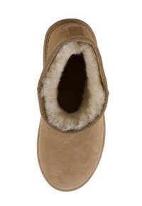 Beżowe zamszowe kapcie z zaokrąglonym czubkiem, podszyte owczą wełną i z ribbowymi materiałowymi akcentami wokół otworu. Miękka tekstura i minimalny design.