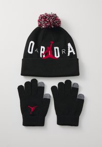 Black knit beanie with a red and white pom-pom on top and bold logo, paired with black gloves featuring gray tips and logo detail.