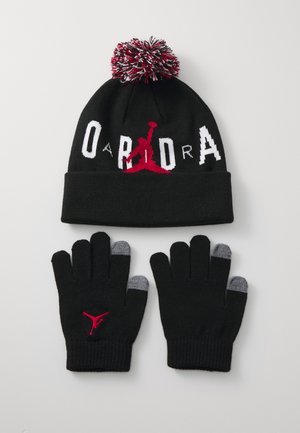 Black knit beanie with a red and white pom-pom on top and bold logo, paired with black gloves featuring gray tips and logo detail.