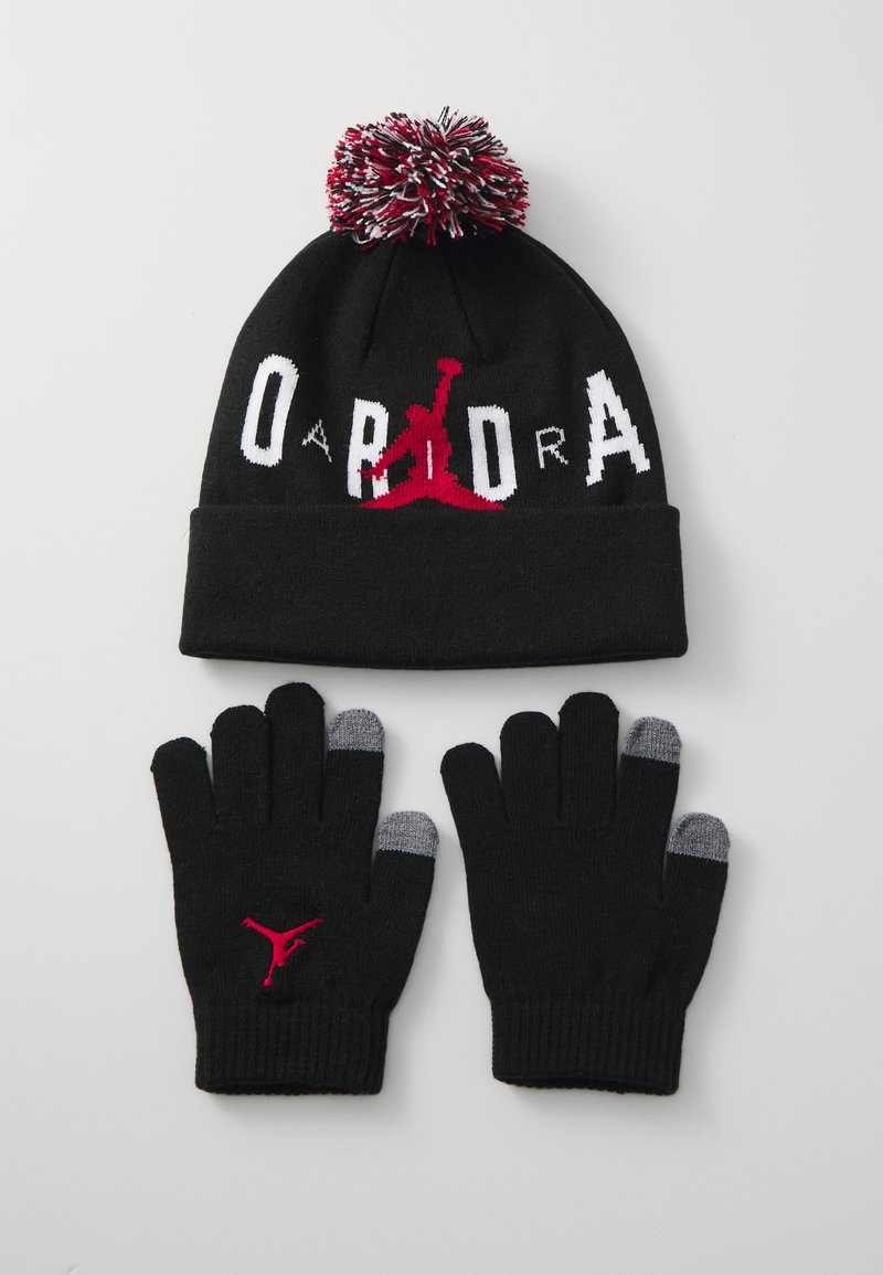 Black knit beanie with a red and white pom-pom on top and bold logo, paired with black gloves featuring gray tips and logo detail.