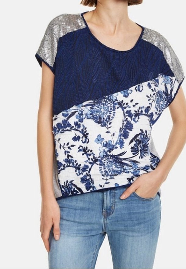 Haut bleu marine avec imprimé floral, manches courtes en sequins argentés et encolure ronde. Le tissu texturé contraste avec les zones plates.